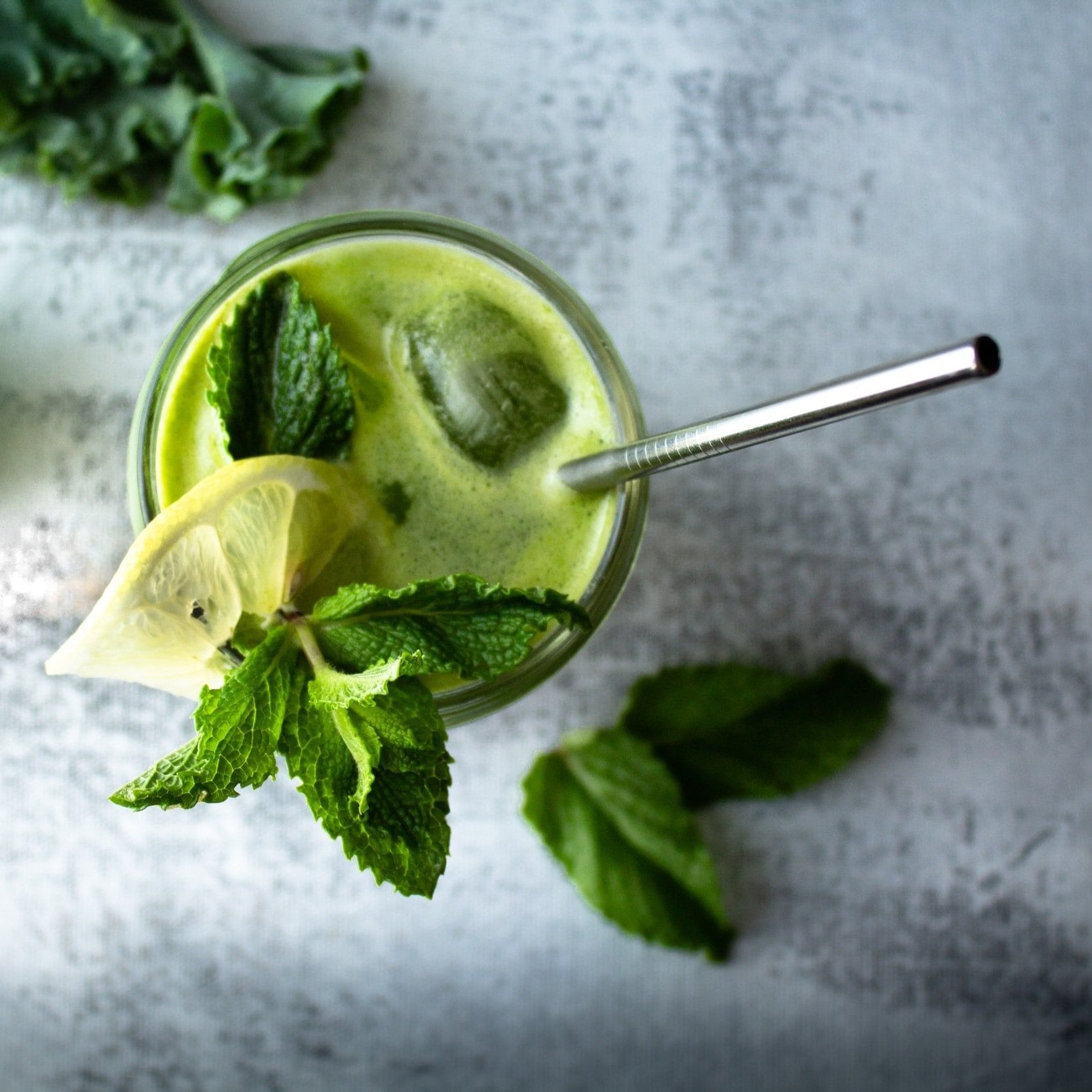 A refreshing glass of green juice with a lemon slice and mint leaves